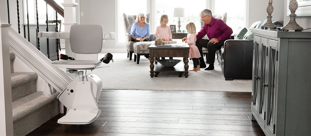Bruno stair lift at bottom of staircase next to living room with people in the background