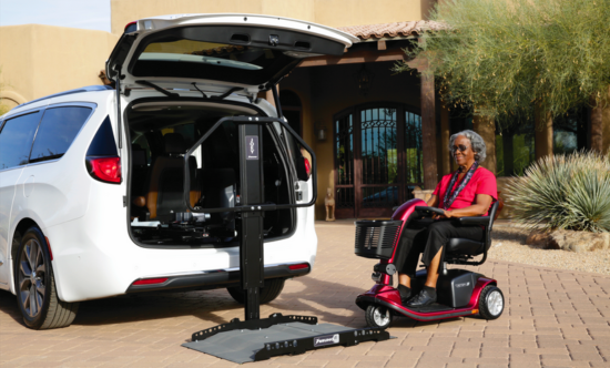 a women driving a scooter onto a scooter lift behind a white van
