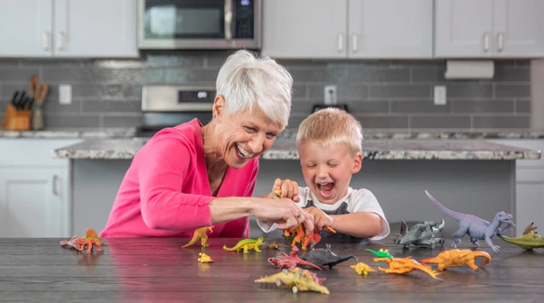 an elderly women and toddler playing with dinosaurs on the kitchen island