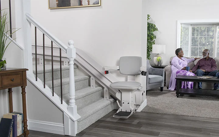 bruno elite curved indoor stair lift with a husband and wife sitting behind it in the living room